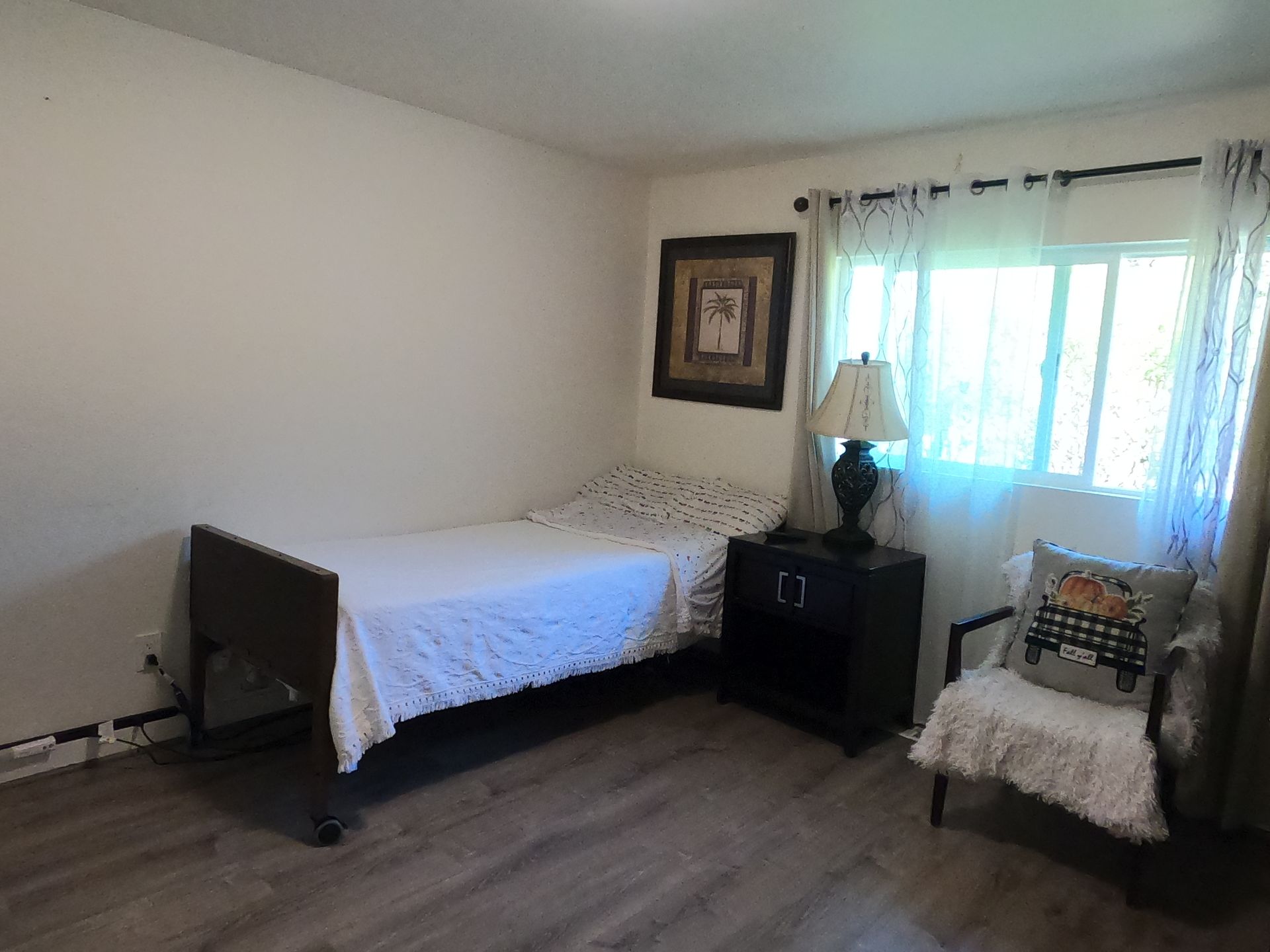 Bedroom with bed, nightstand, chair, window with curtains, and artwork on wall.