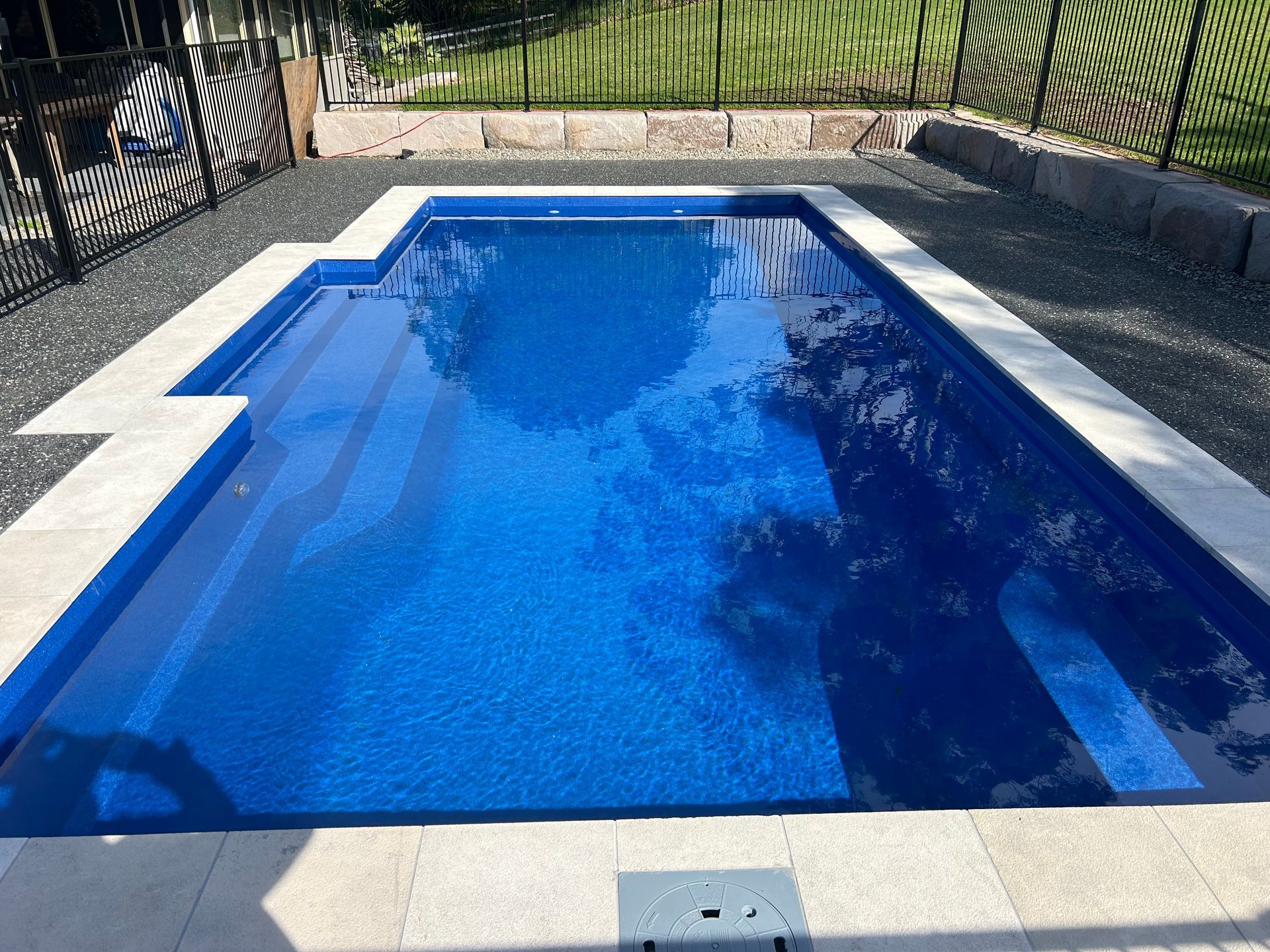 A large blue swimming pool is surrounded by a fence. — Steve Merrick Family Swimming Pools in Diamond Beach, NSW