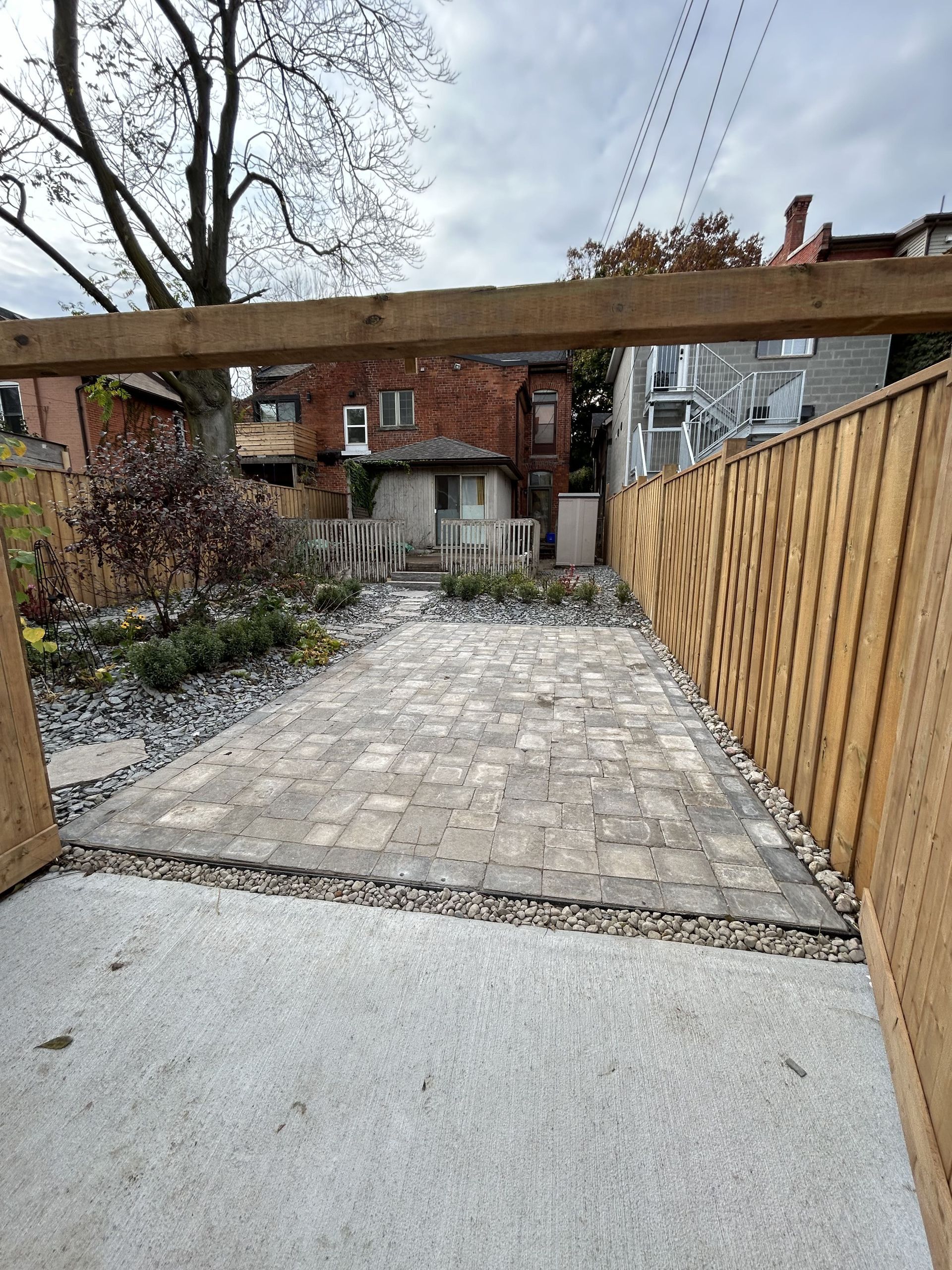 A wooden fence surrounds a brick walkway in a backyard.