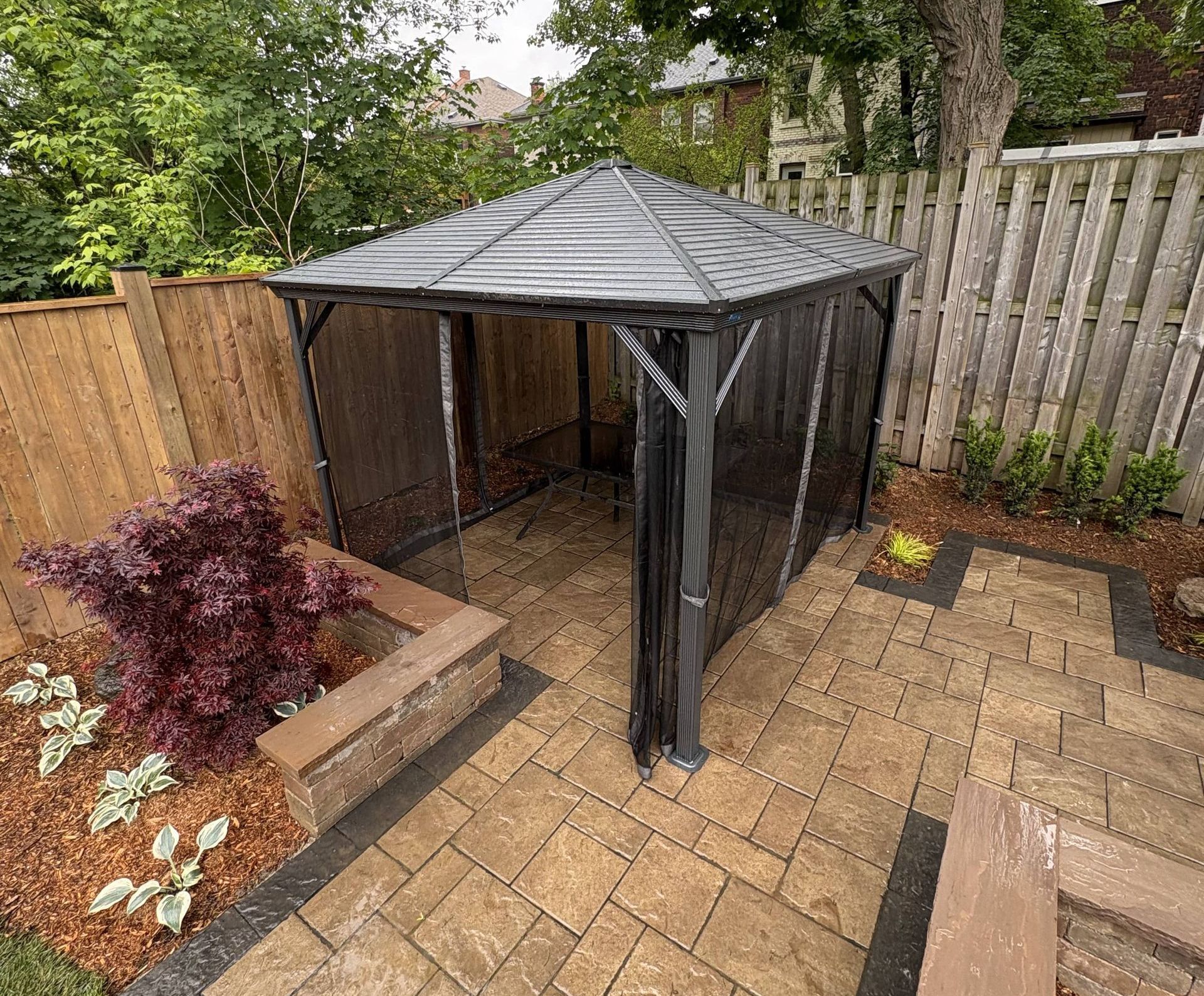 A gazebo is sitting on top of a brick patio next to a wooden fence.