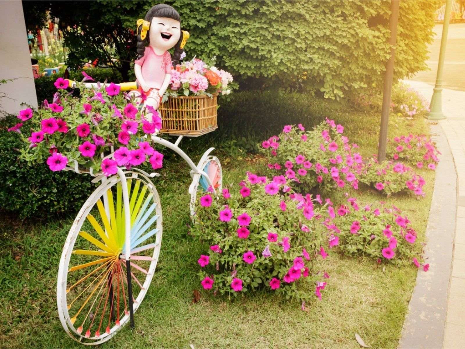 A bicycle with a basket of pink flowers and a doll on it.
