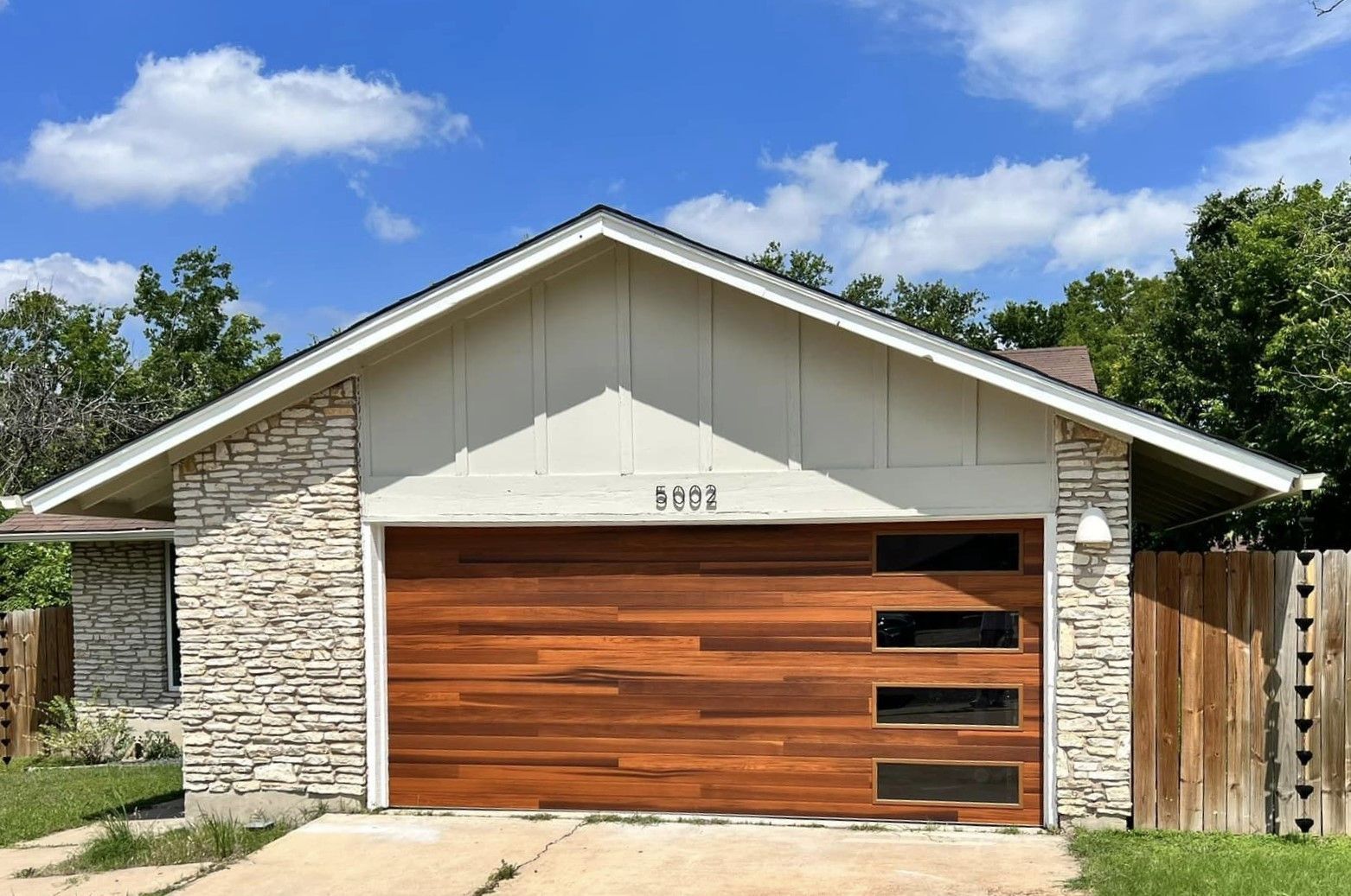 A house with a wooden garage door and a stone wall.