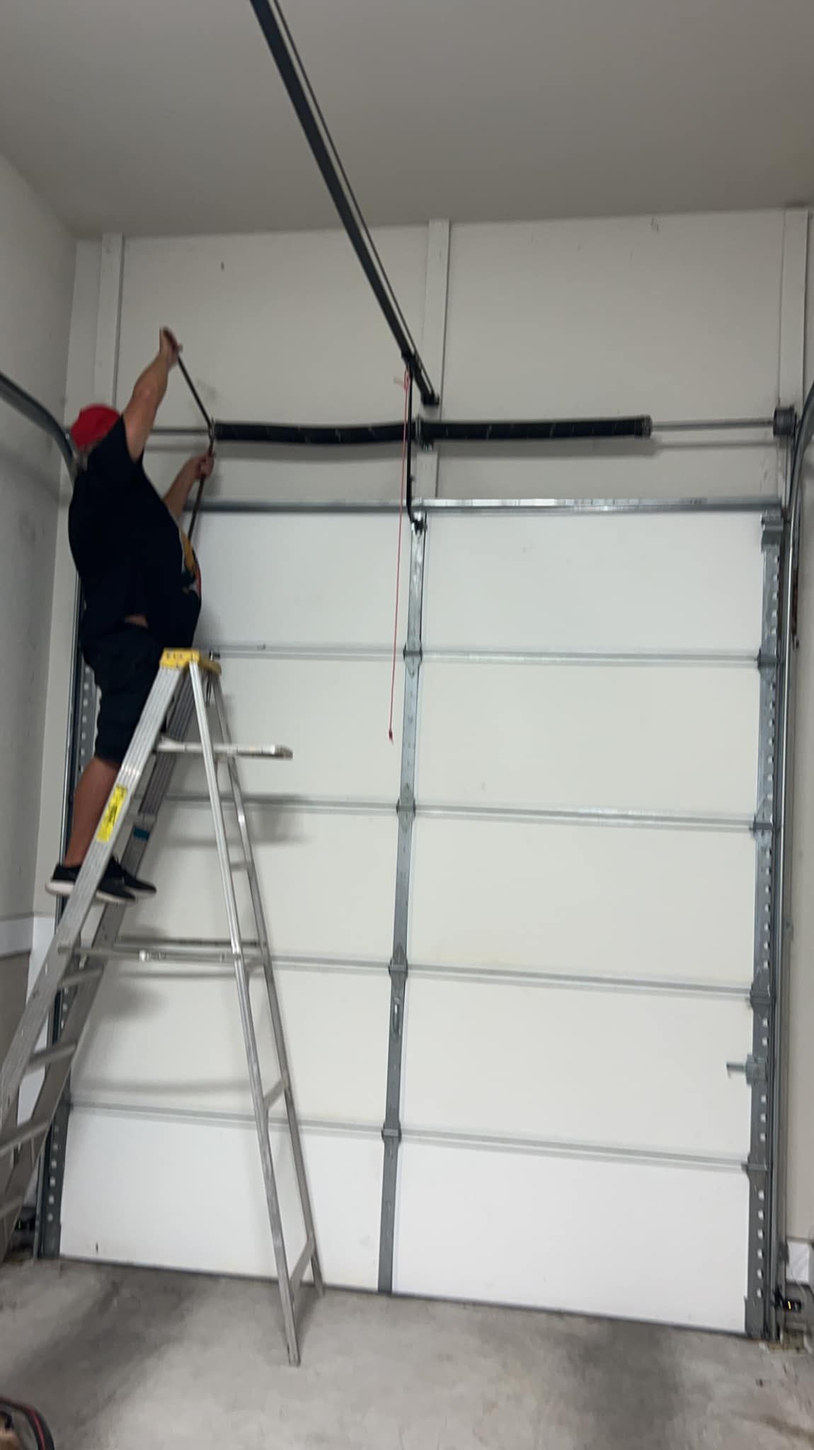 A man is standing on a ladder fixing a garage door.