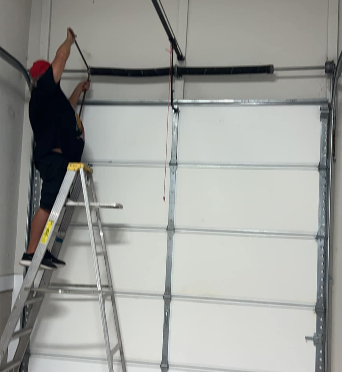 A man is standing on a ladder fixing a garage door.