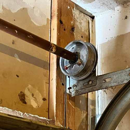 A close up of a garage door pulley on a wooden wall.