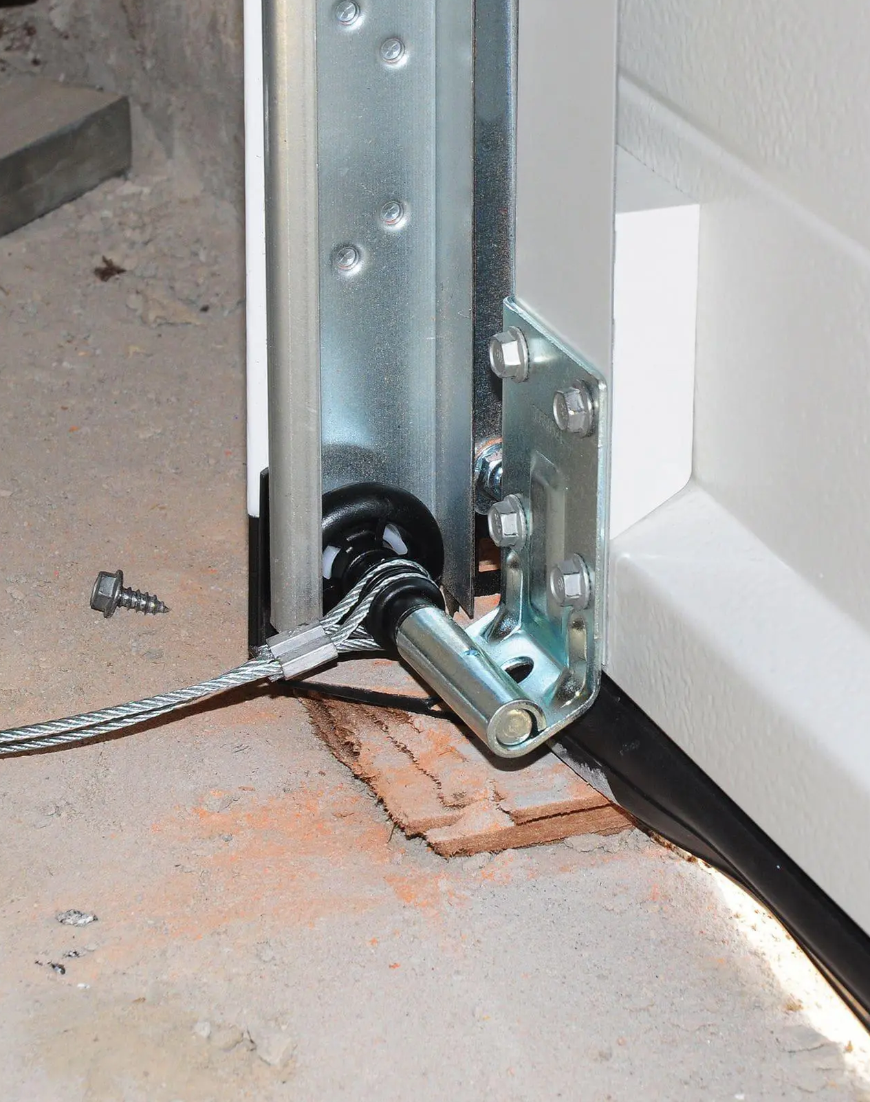 Close-up of a garage door roller inside metal track with hinge bracket and mounting bolts