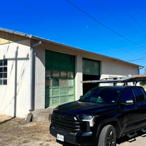 A black truck is parked in front of a white building.