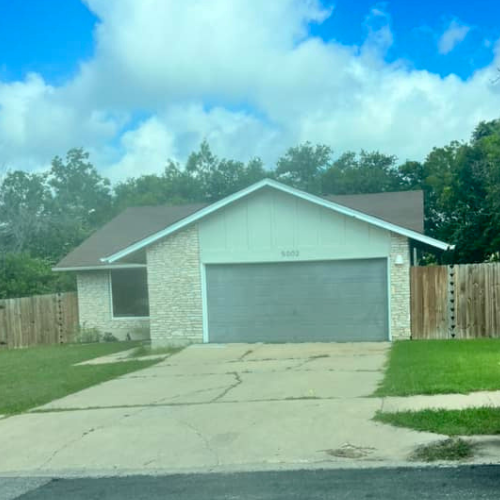 A white house with a gray garage door and a wooden fence