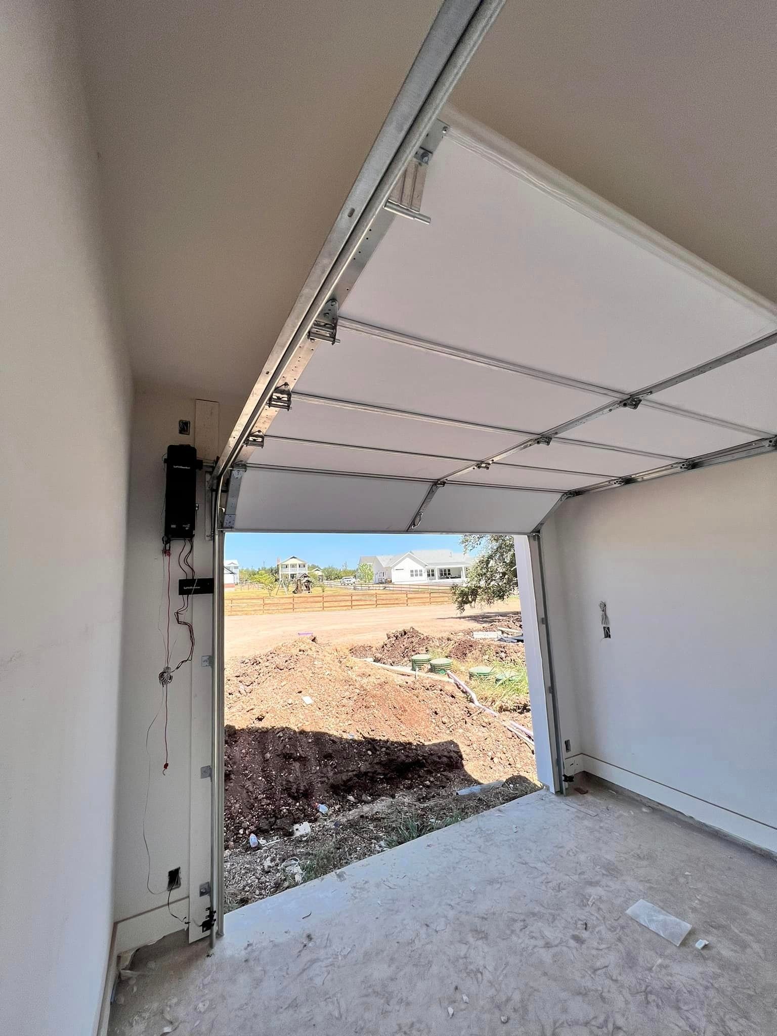 A garage door is open and looking out to a dirt field.