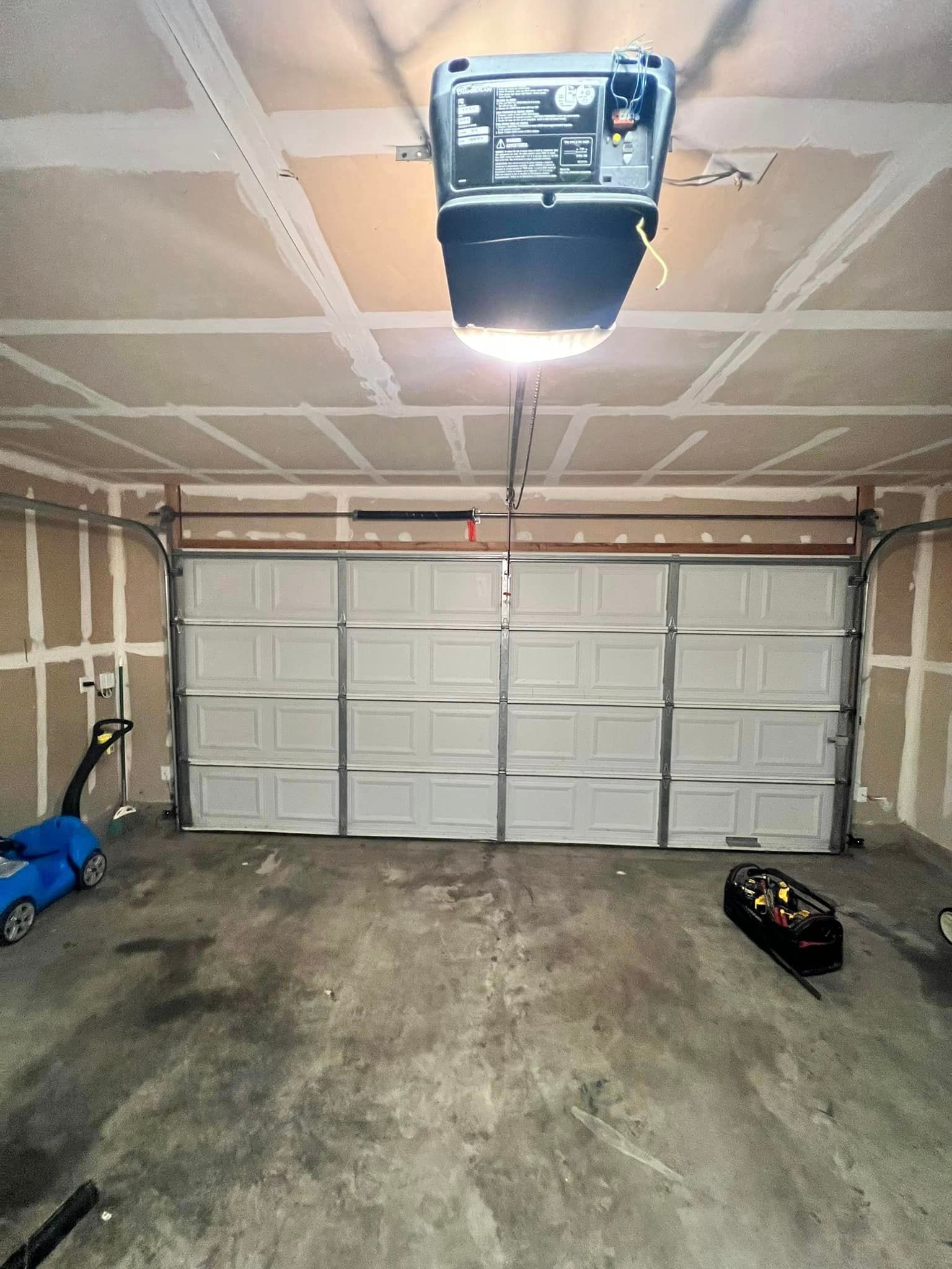 Garage interior with closed white garage door, overhead opener, and concrete floor.