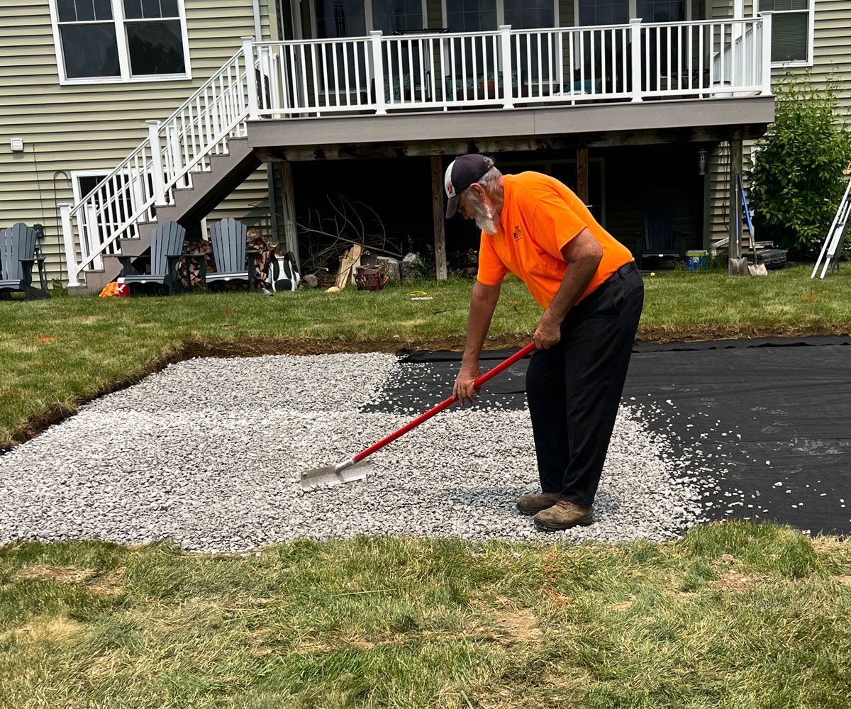 A crew member at Chidsey Landscape & Design grading gravel foundation for paver patio in Medina, Ohio backyard.
