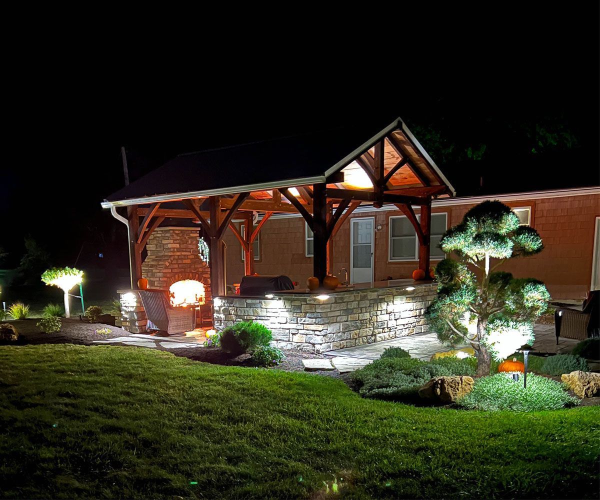 Landscape outdoor lighting in Fairlawn, Ohio backyard patio pavilion with tree uplighting and outdoor kitchen cabinet exterior lighting.