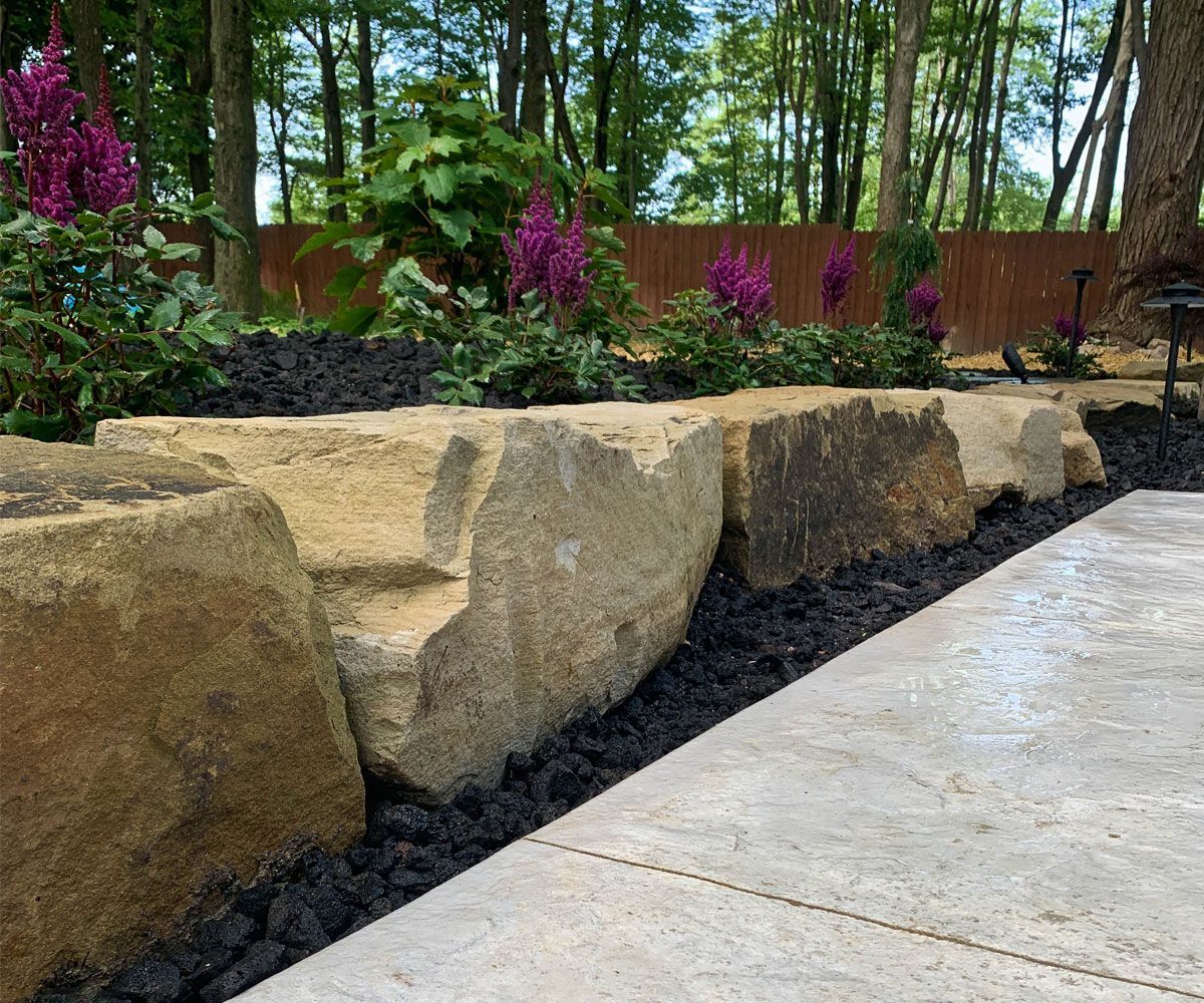Natural stone outcropping boulders being used as a landscape retaining wall in Fairlawn, Ohio backyard.