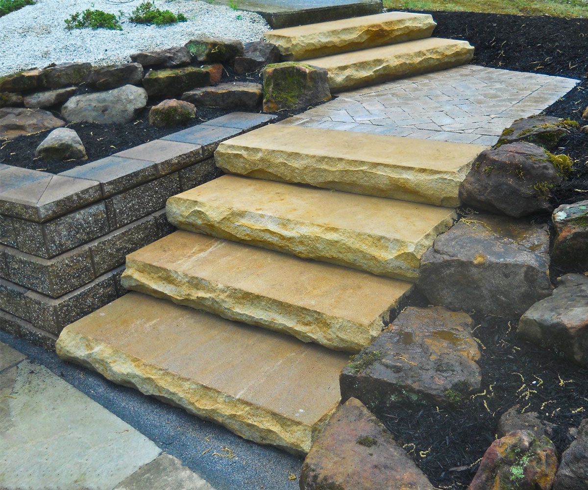 Natural sandstone steps connecting landscape tiers with wall block retaining wall in Lorain County backyard home.