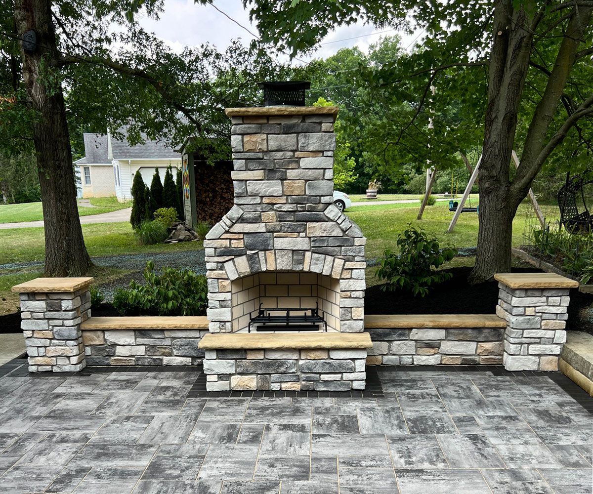 Outdoor stone fireplace with chimney, hearth, and seating wall pillars on Northeast Ohio backyard  Unilock paver patio.