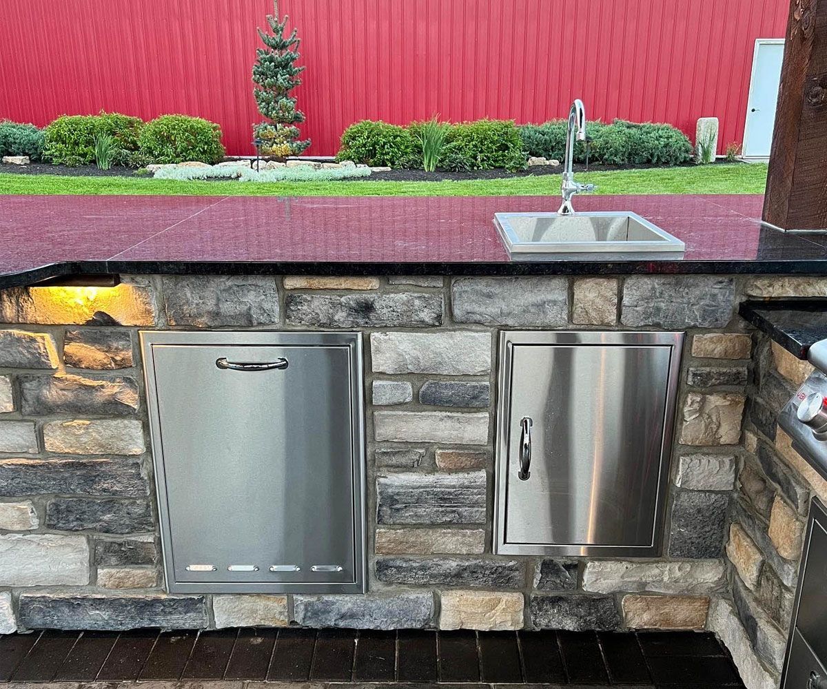 Custom outdoor kitchen cabinets with buil-in sink, outdoor refrigerator, and trash drawer in Bath, Ohio patio by Chidsey Landscape & Design