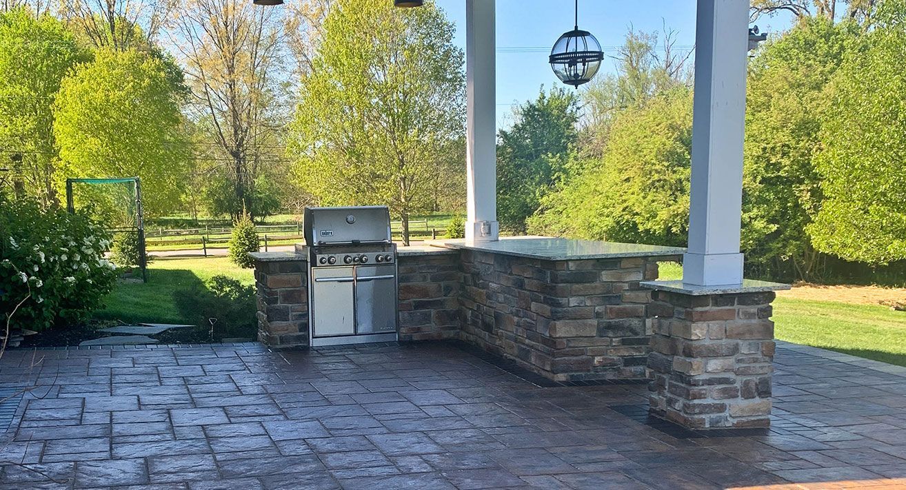 Custom outdoor kitchen under pavilion in Northeast Ohio with built-in gas grill and stone pillars.