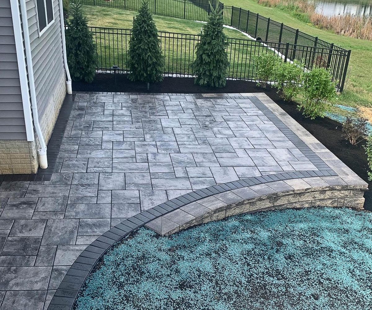 New paver patio with dark paver border and retaining wall on sloped backyard in Medina County, OH