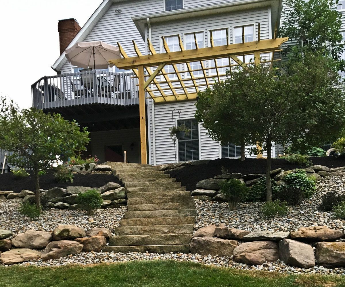 Grand spiral outdoor staircase made from natural landscape stone with tiered natural outcropping retaining walls of Northeast Ohio home
