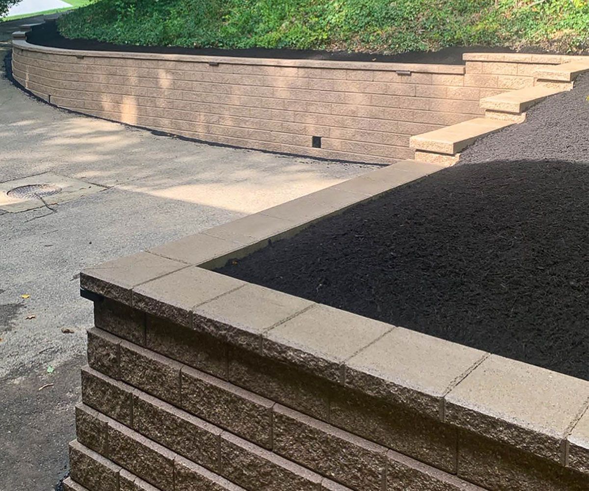 Paving wall block stone retaining wall on sloped front yard by Bath, OH driveway to help with water runoff and soil erosion.