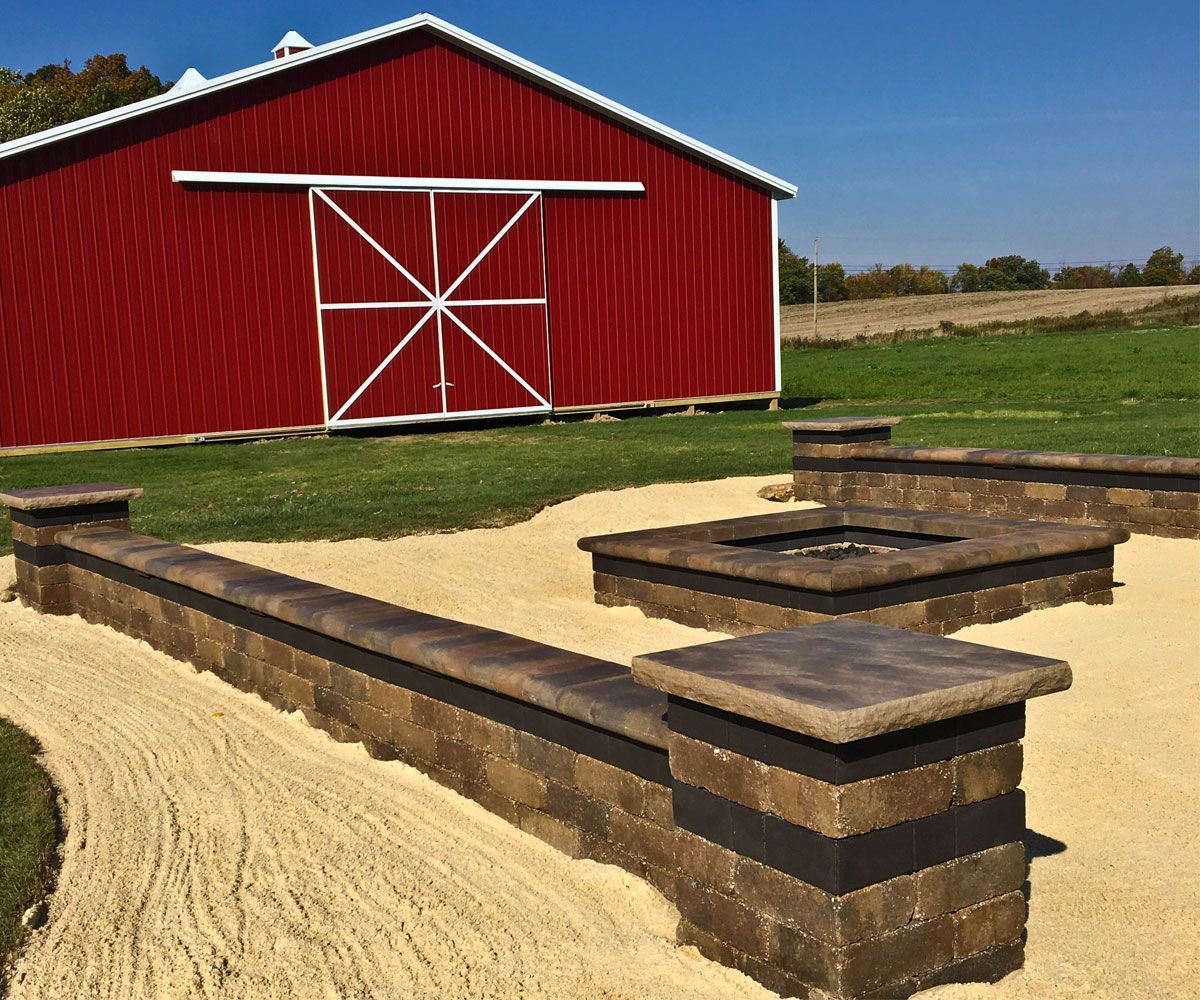 Medina, Ohio backyard with low stone seating wall, pillars, and wall lighting for additional seating by custom fire pit by Chidsey Landscape & Design