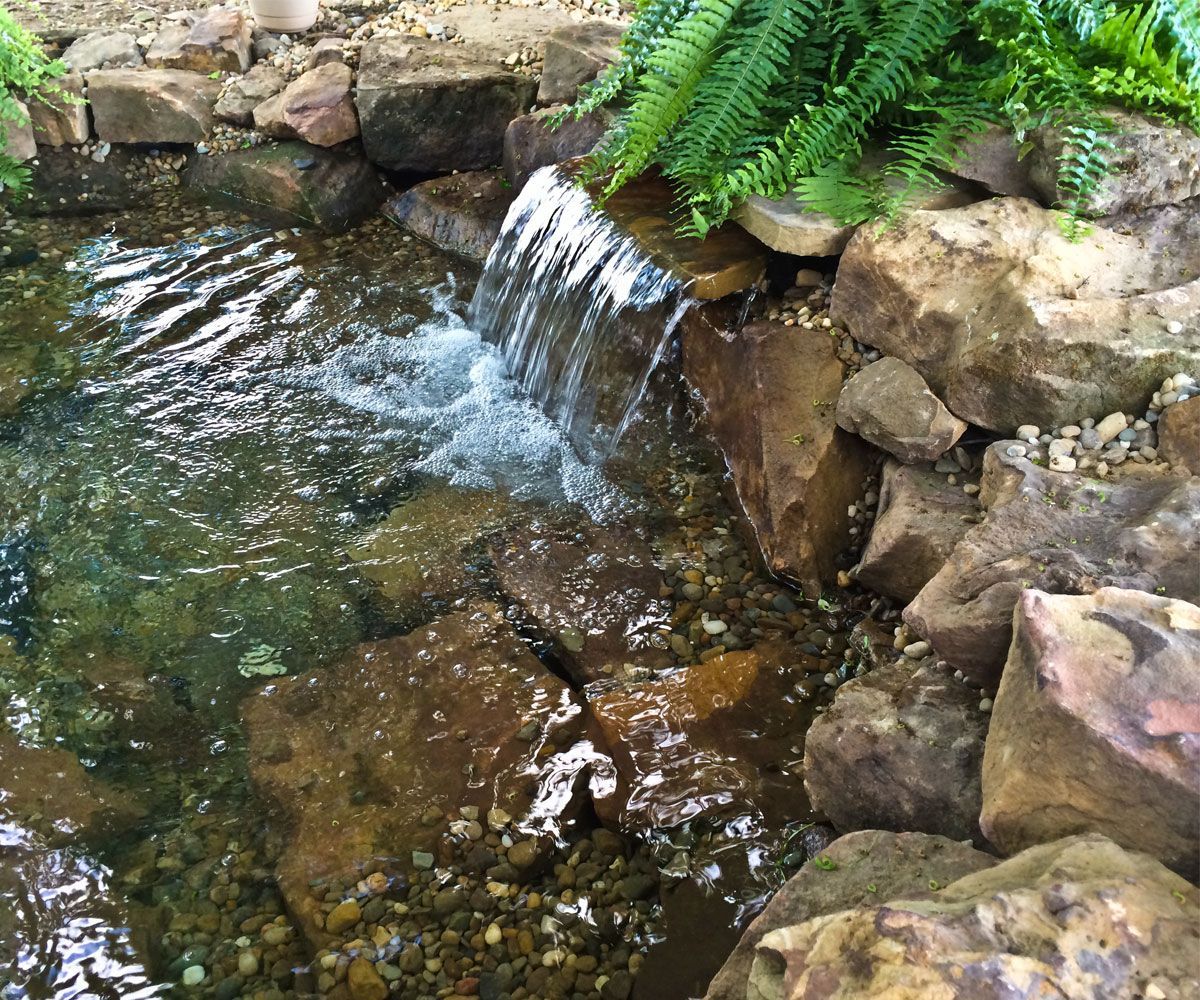 Sheer waterfall in backyard Northeast Ohio landscape with natural landscape stone boulders, surrounded by lush plantings.
