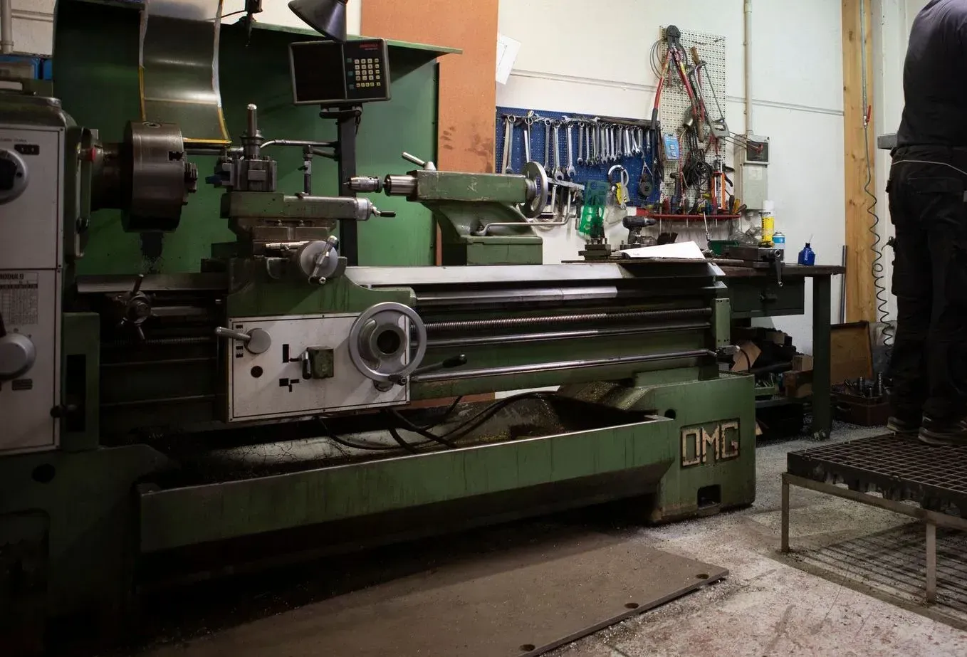 Officina industriale con grandi macchinari verdi e un operaio che aziona le attrezzature sulla destra.