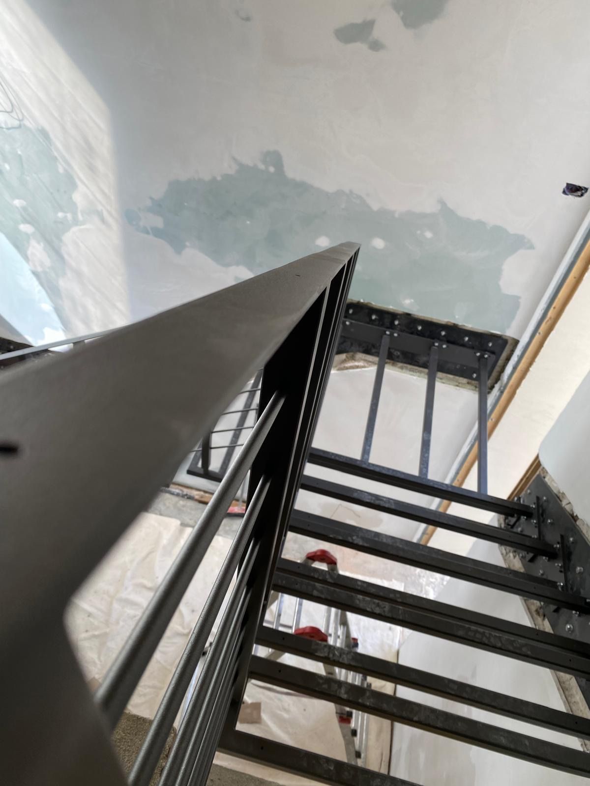 Scala metallica che sale all'interno di un edificio con pareti non rifinite e ringhiera nera.