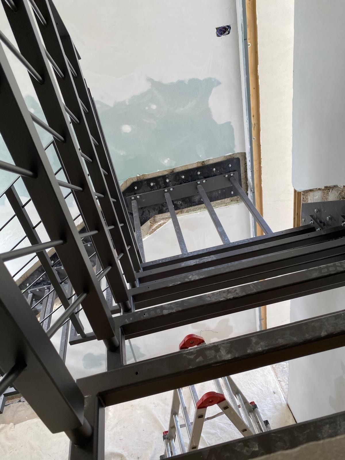 Un operaio su una scala ripara il soffitto sopra le travi metalliche nere di una scala.