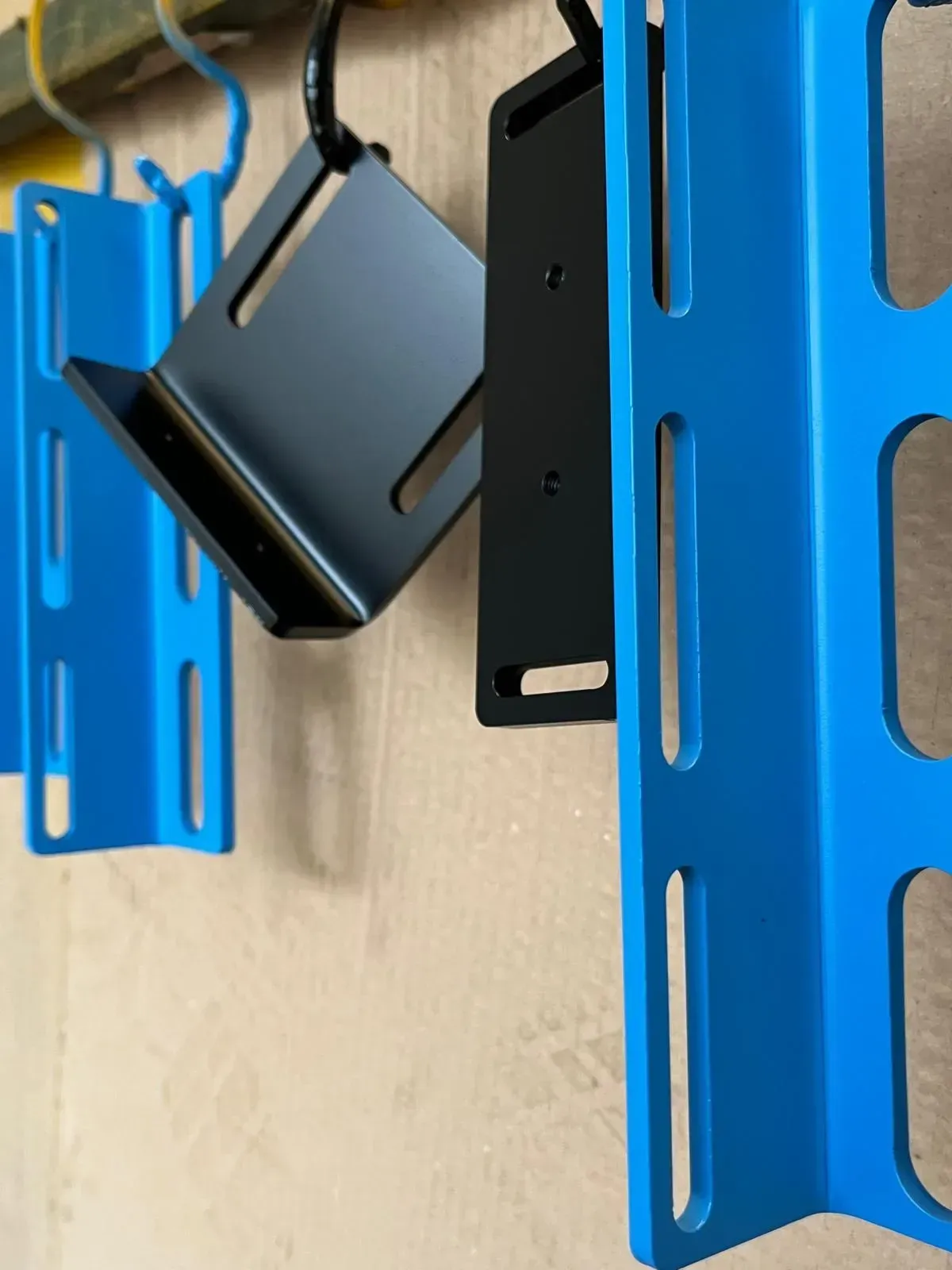 Primo piano di un dispositivo nero montato tra staffe metalliche blu su una parete beige.