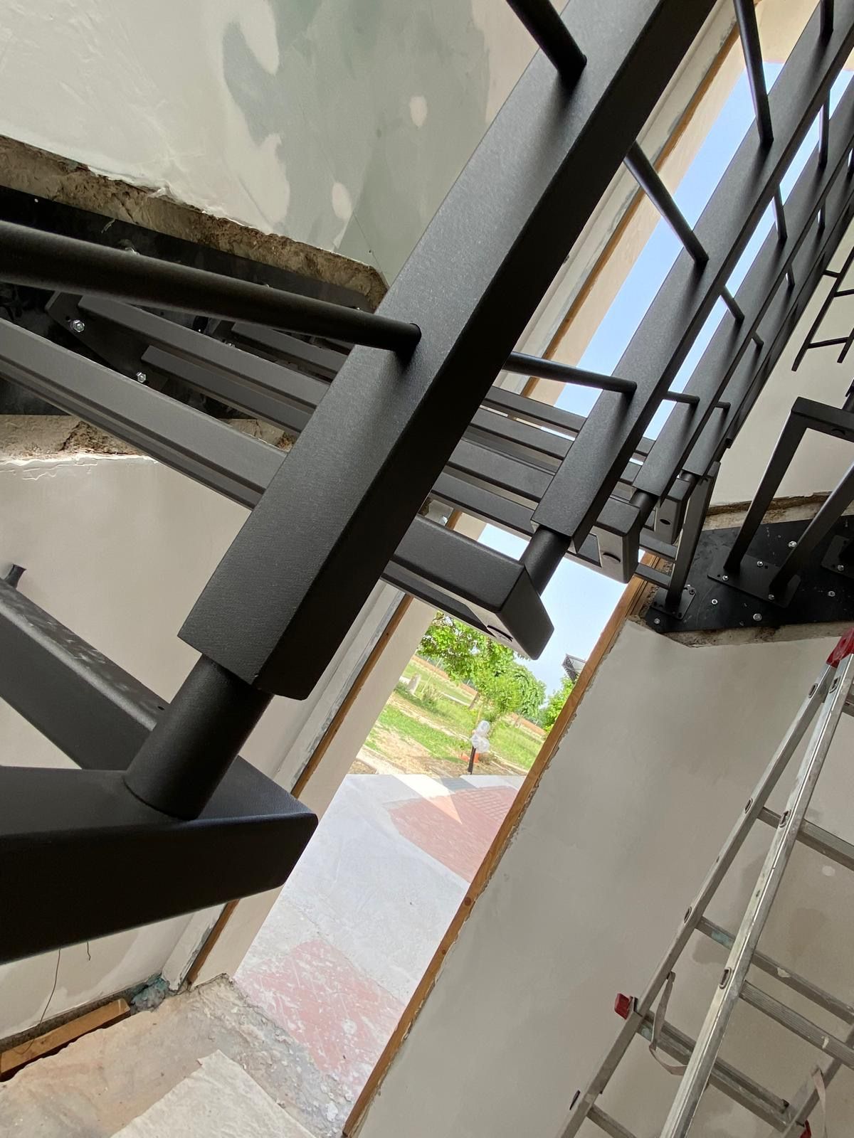 Vista inclinata di una tromba delle scale con ringhiere in metallo nero, pareti bianche e una scala a pioli accanto a un pianerottolo aperto.