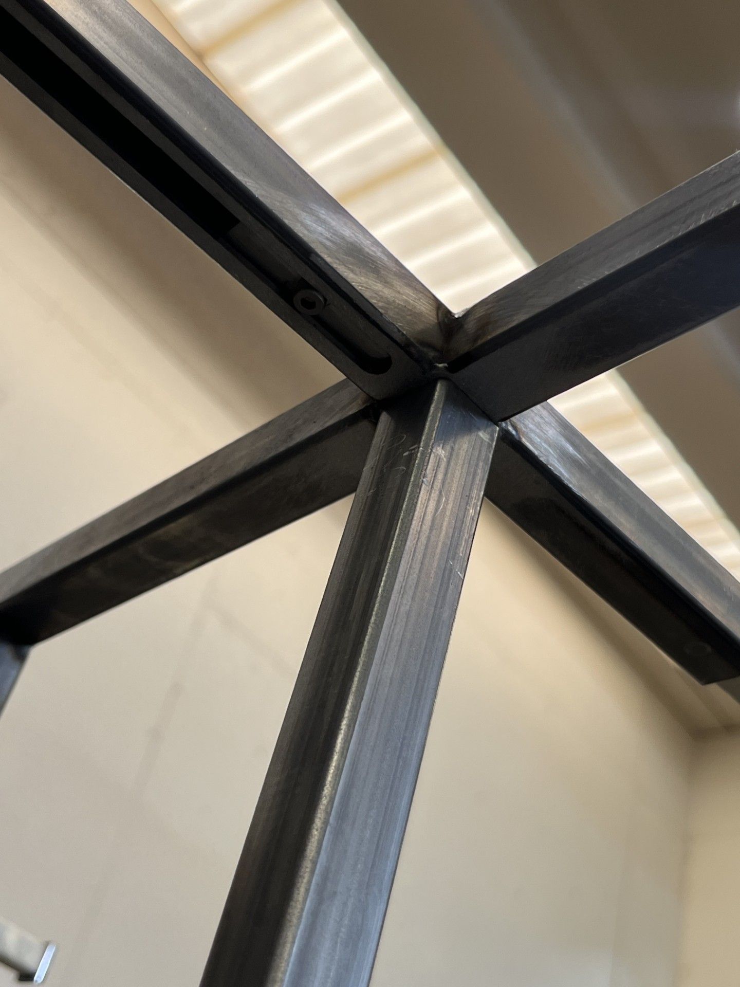 Primo piano di travi metalliche scure che formano una X su un soffitto con un lucernario sopra.