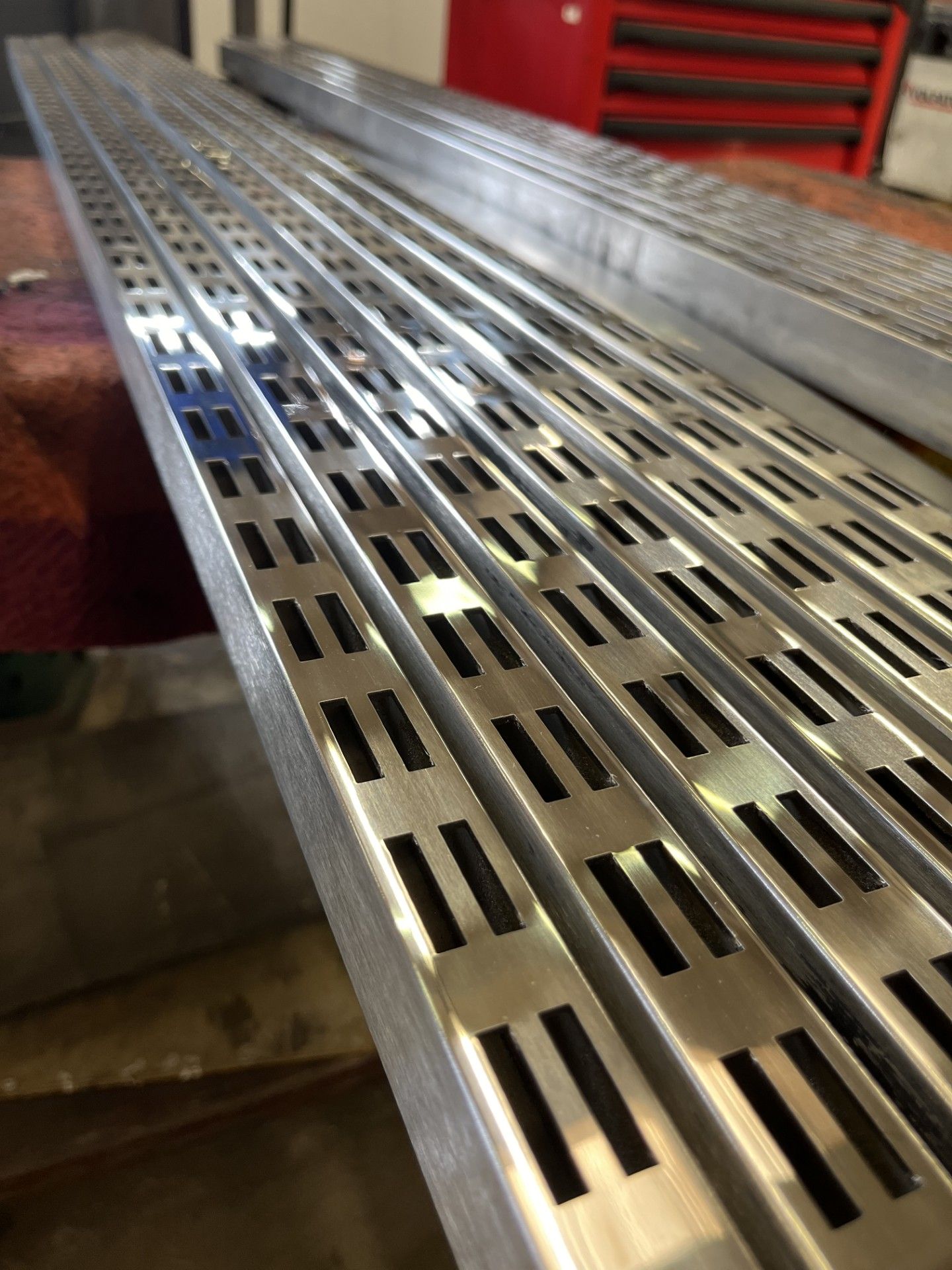 Grigliato metallico perforato su una superficie industriale, con sedute rosse sullo sfondo.