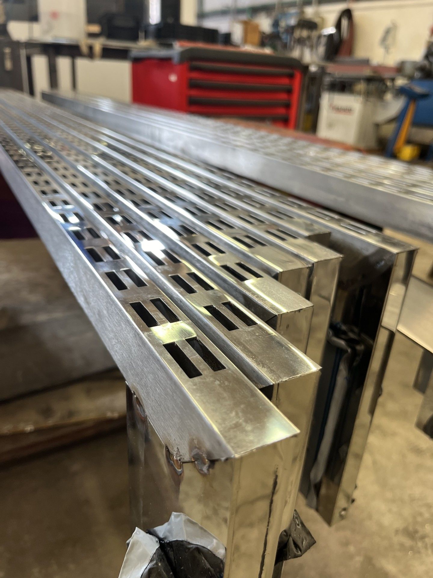 Barre metalliche scanalate impilate in un'officina, che mostrano in primo piano le estremità lucide e lavorate.