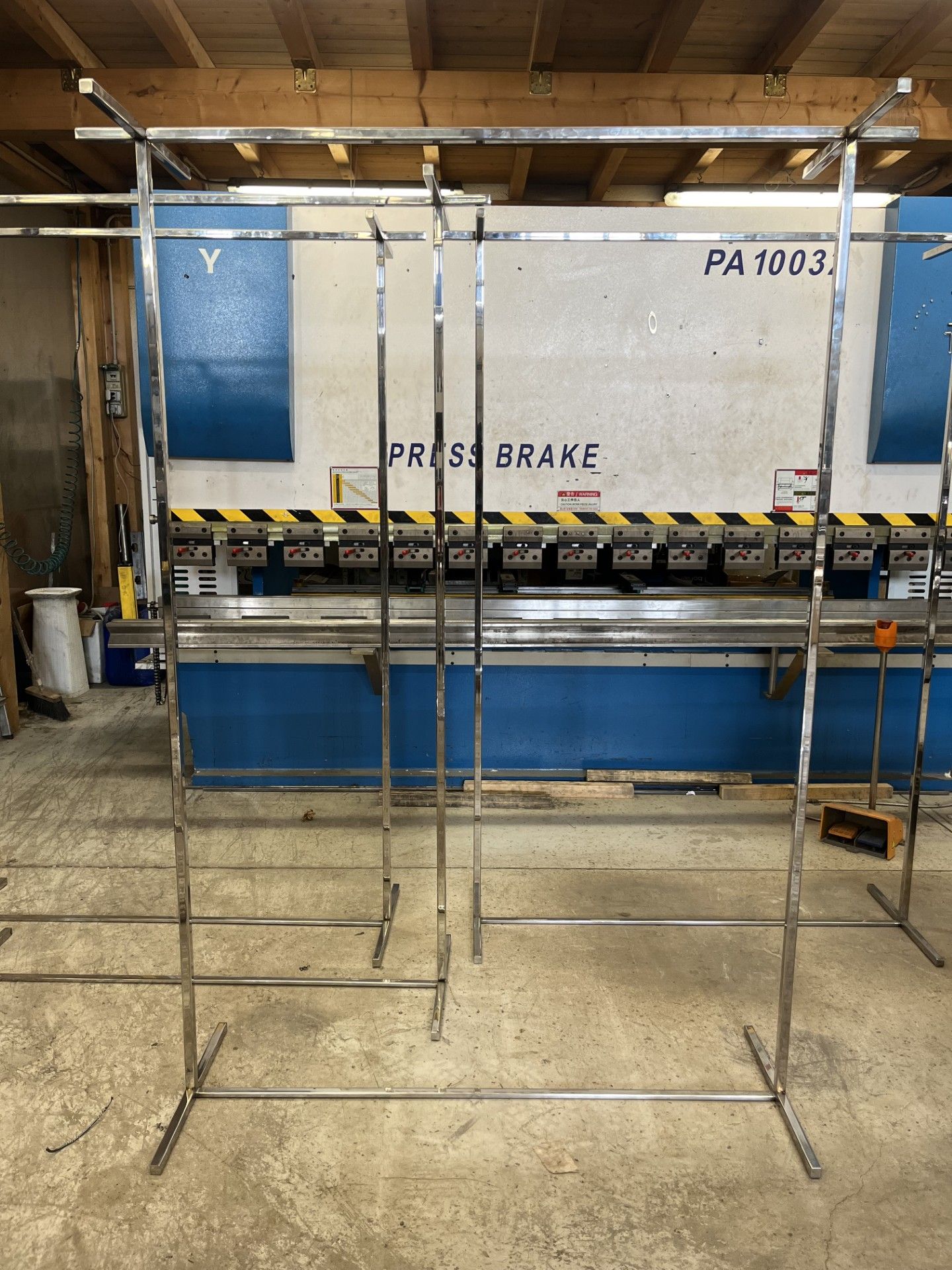 Telaio di prova metallico in un magazzino, con una pressa piegatrice e pannelli blu sullo sfondo.
