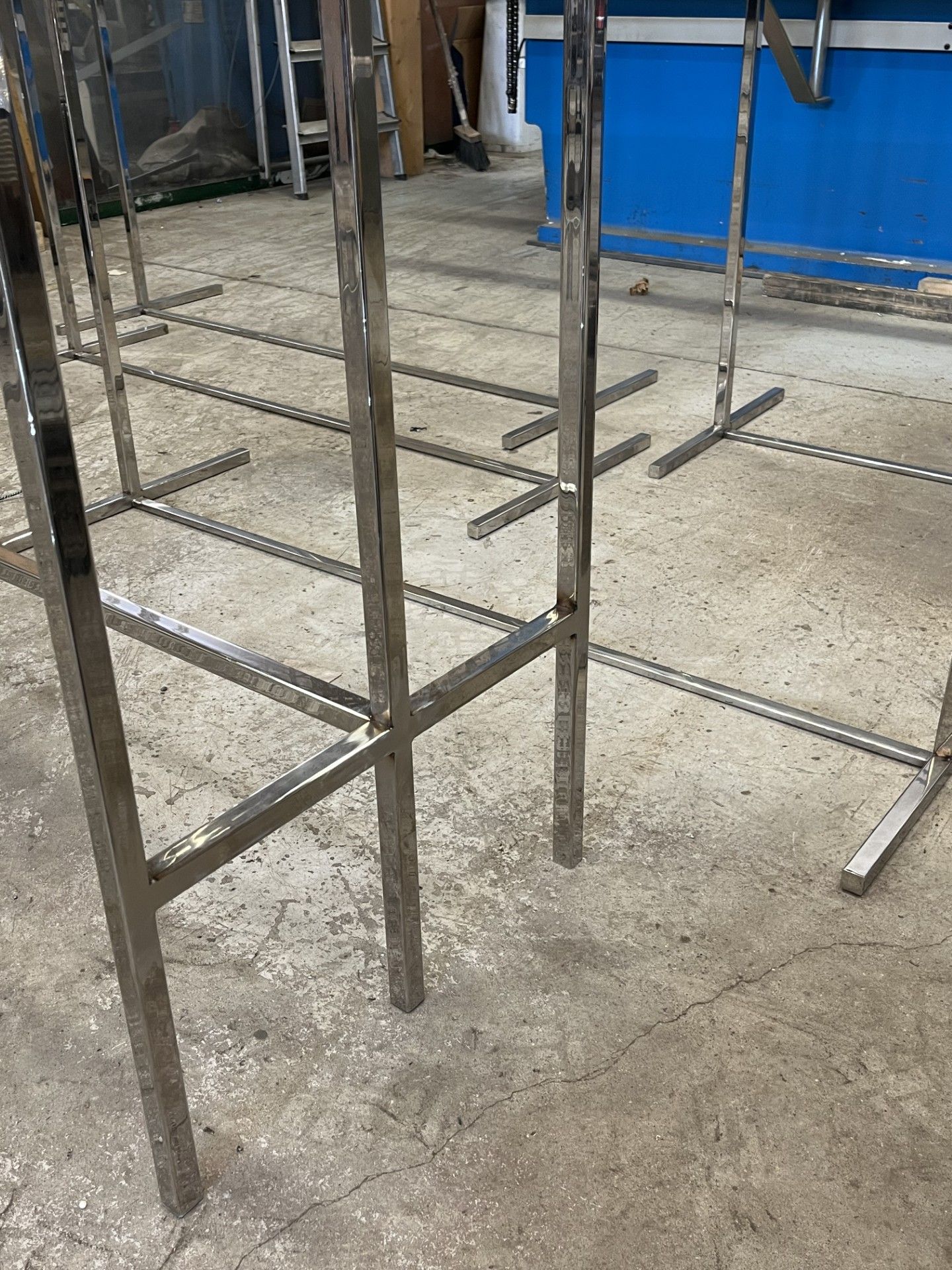 Struttura di ponteggio metallico su un pavimento di cemento in un cantiere al coperto, con un telo blu sullo sfondo.