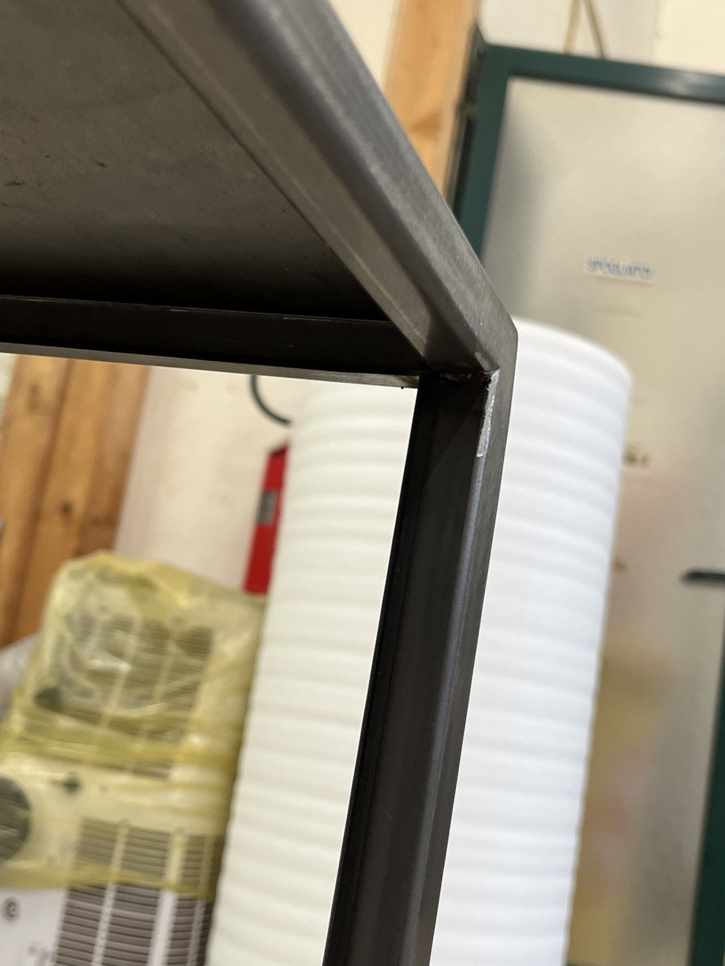 In primo piano, in una stanza simile a un'officina, si vede una mensola in metallo nero con un elettrodomestico beige e un estintore rosso.