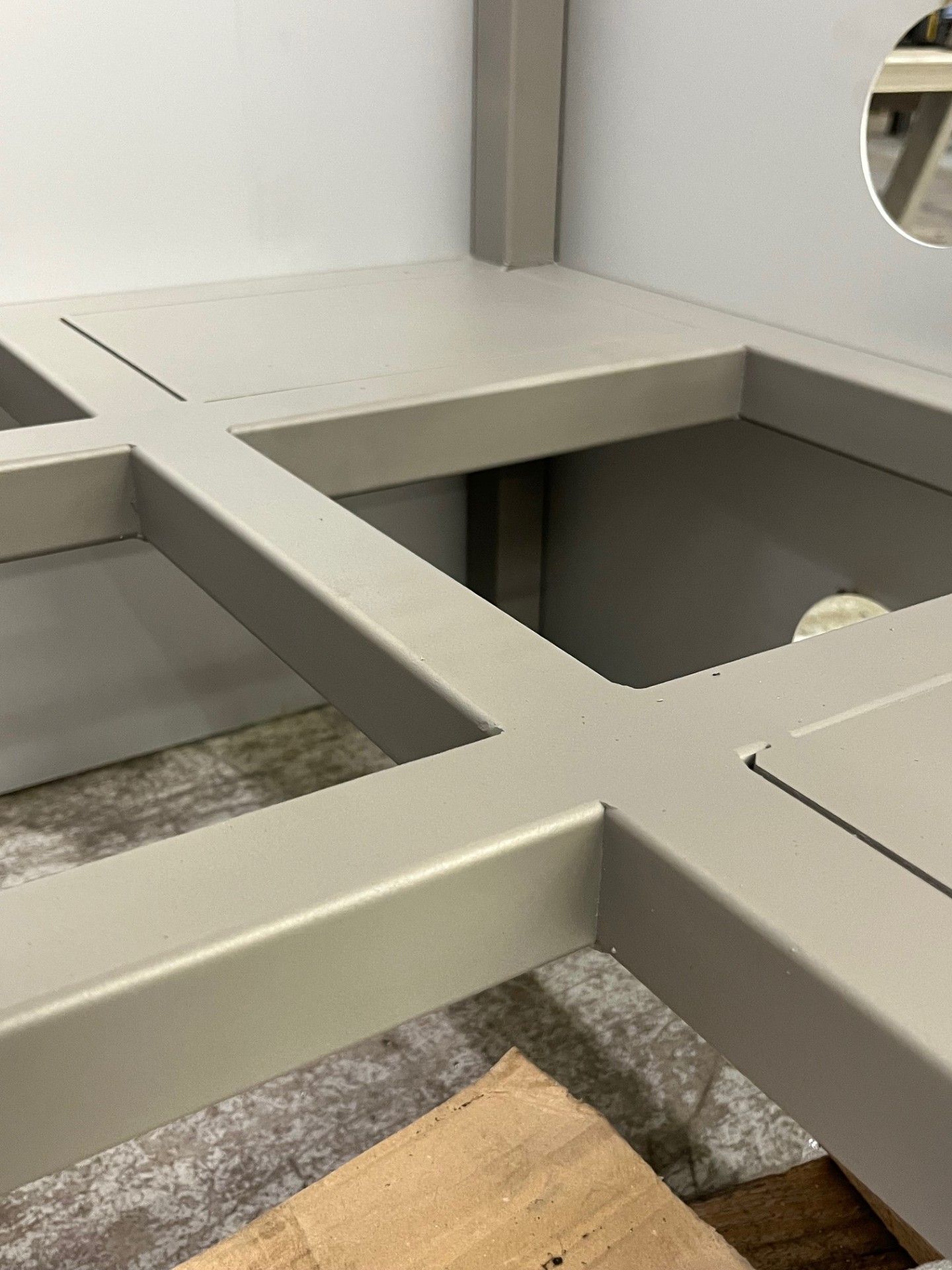 Un tavolo modulare grigio incornicia un'ampia apertura quadrata in una stanza con pavimento in moquette e legno.