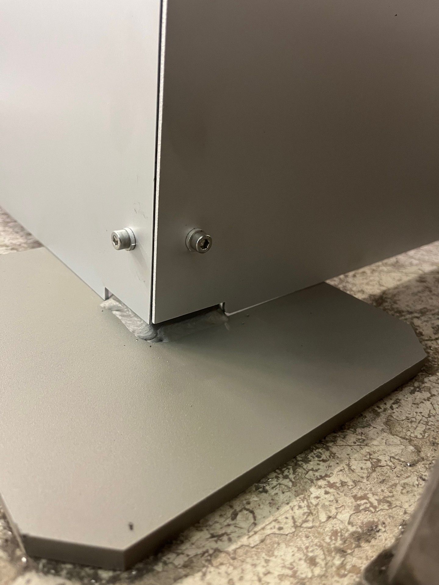 Primo piano di una piastra di base in metallo grigio e di un pannello verticale montati su un pavimento rivestito di moquette.