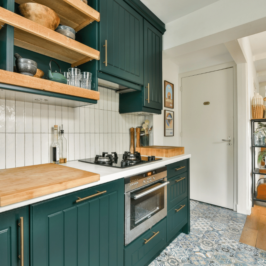 Modern kitchen with dark green cabinets, wood shelves, white tile backsplash, and patterned tile floor