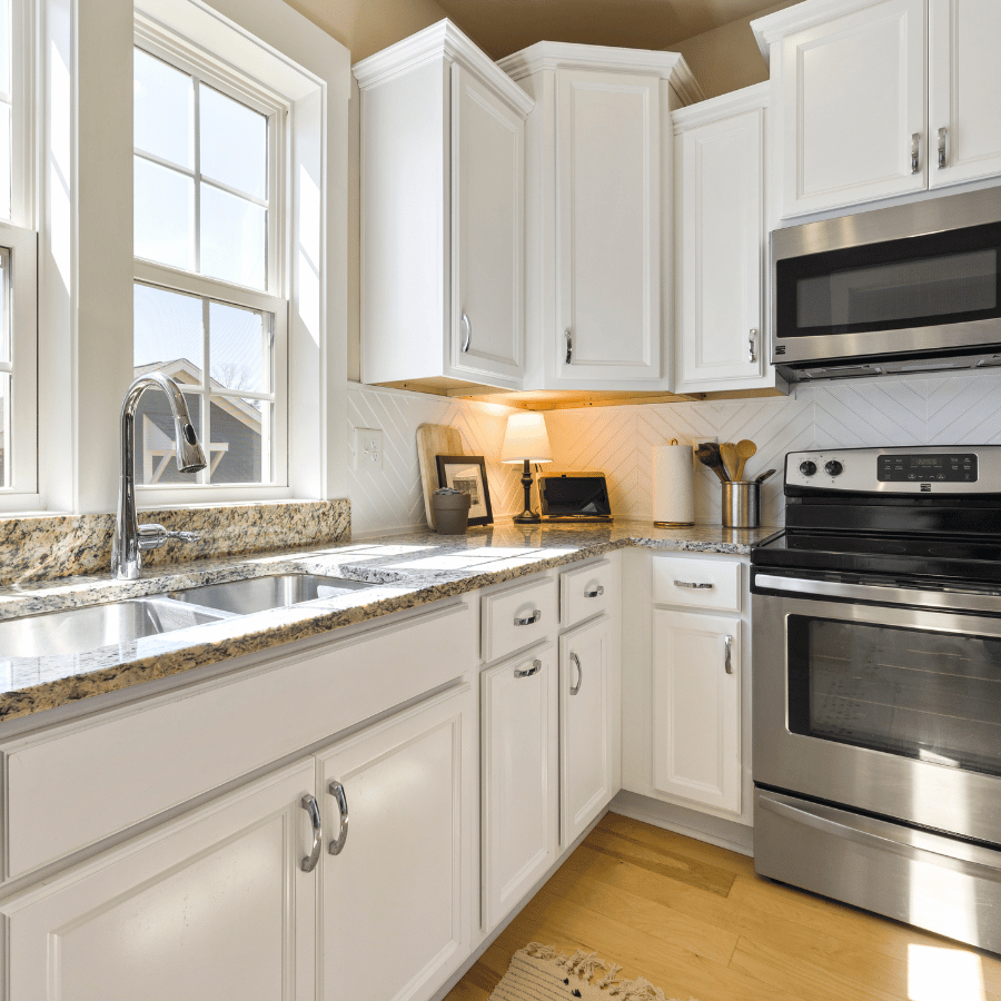 Bright white modern kitchen with island, white cabinets, stove, and large window.