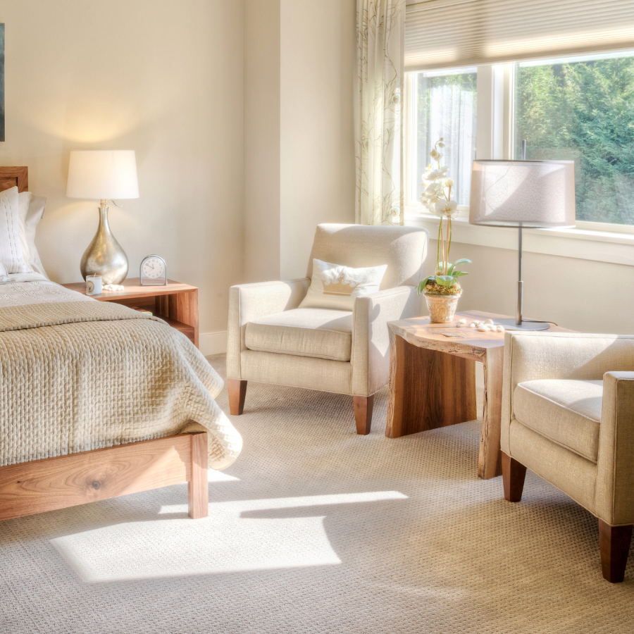 Bright bedroom with beige chairs, wooden side tables, bed, and sunlight from a window
