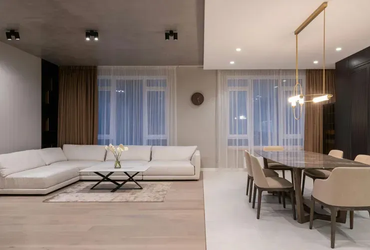 Modern open-plan living and dining room with white sectional sofa, wood table, and floor-to-ceiling windows