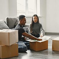 Two people unpacking boxes in a bright living room with a couch and large window
