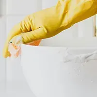 Yellow-gloved hand cleaning a white bowl with a sponge