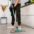 Person mopping a kitchen floor with a turquoise spray mop, wearing black pants and white sneakers