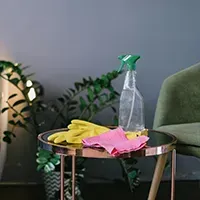 Cleaning supplies on a glass table beside a green chair, with yellow gloves and pink cloths.