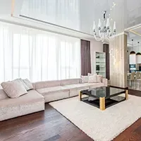 Bright modern living room with white sectional sofa, chandelier, glass coffee table, and large windows