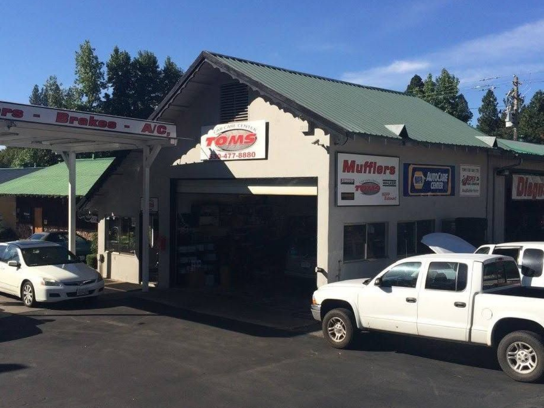 Auto repair shop exterior with parked white vehicles and a green roof under a clear sky | Tom's Car Care