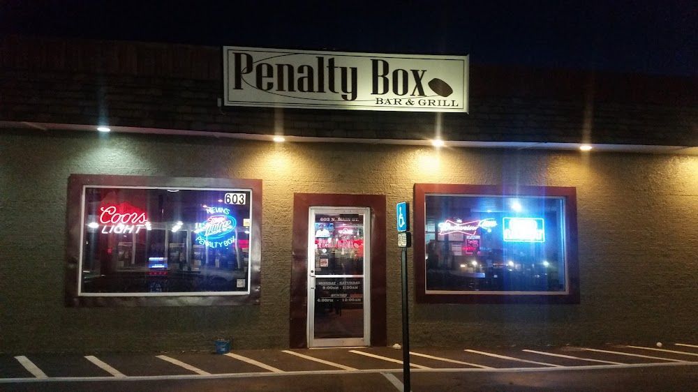 Night view of Penalty Box storefront with neon-lit windows and a central door.